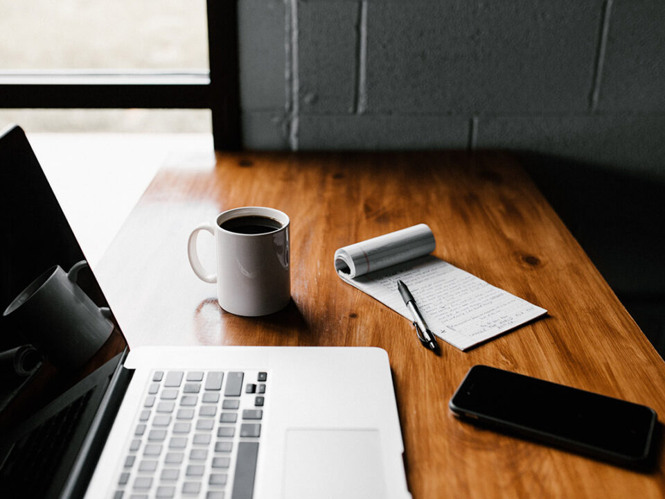 desk with laptop, coffee, notes and cellphone on top