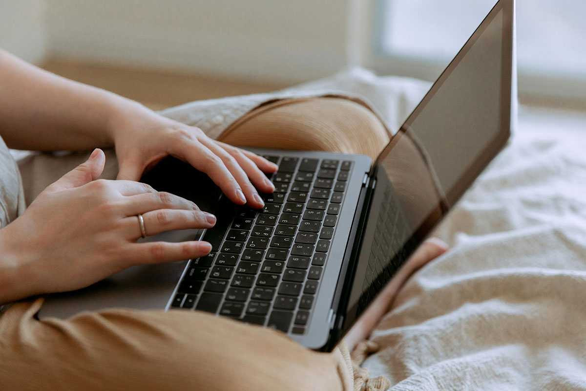 woman sitting on a bed typing on a laptop